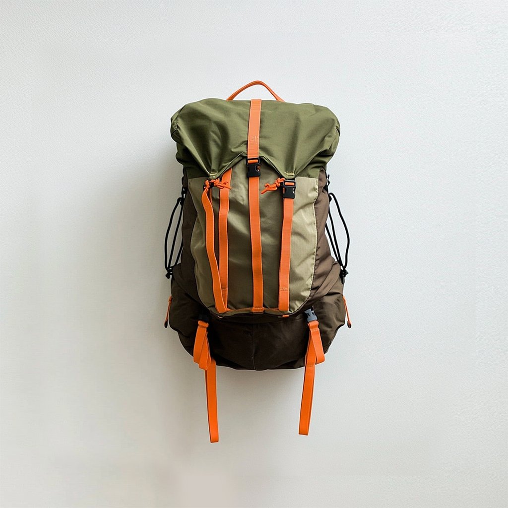 An e-commerce product image of a hiking backpack on the yellowish withered grass covered with brown fallen leaves right next to a forest. 